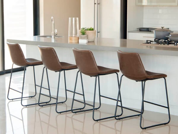 Modern kitchen setting with four counter chairs made of brown faux leather and black metal supports as well as a footrest